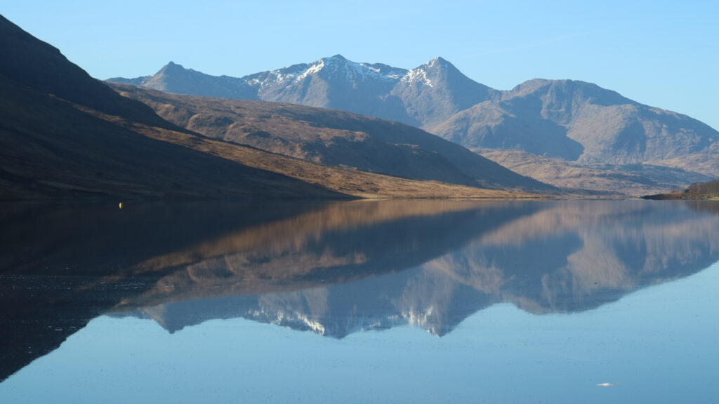 Colour photo of Loch Etive on a calm, cloudless day. Ben Cruachan reflected in the water.